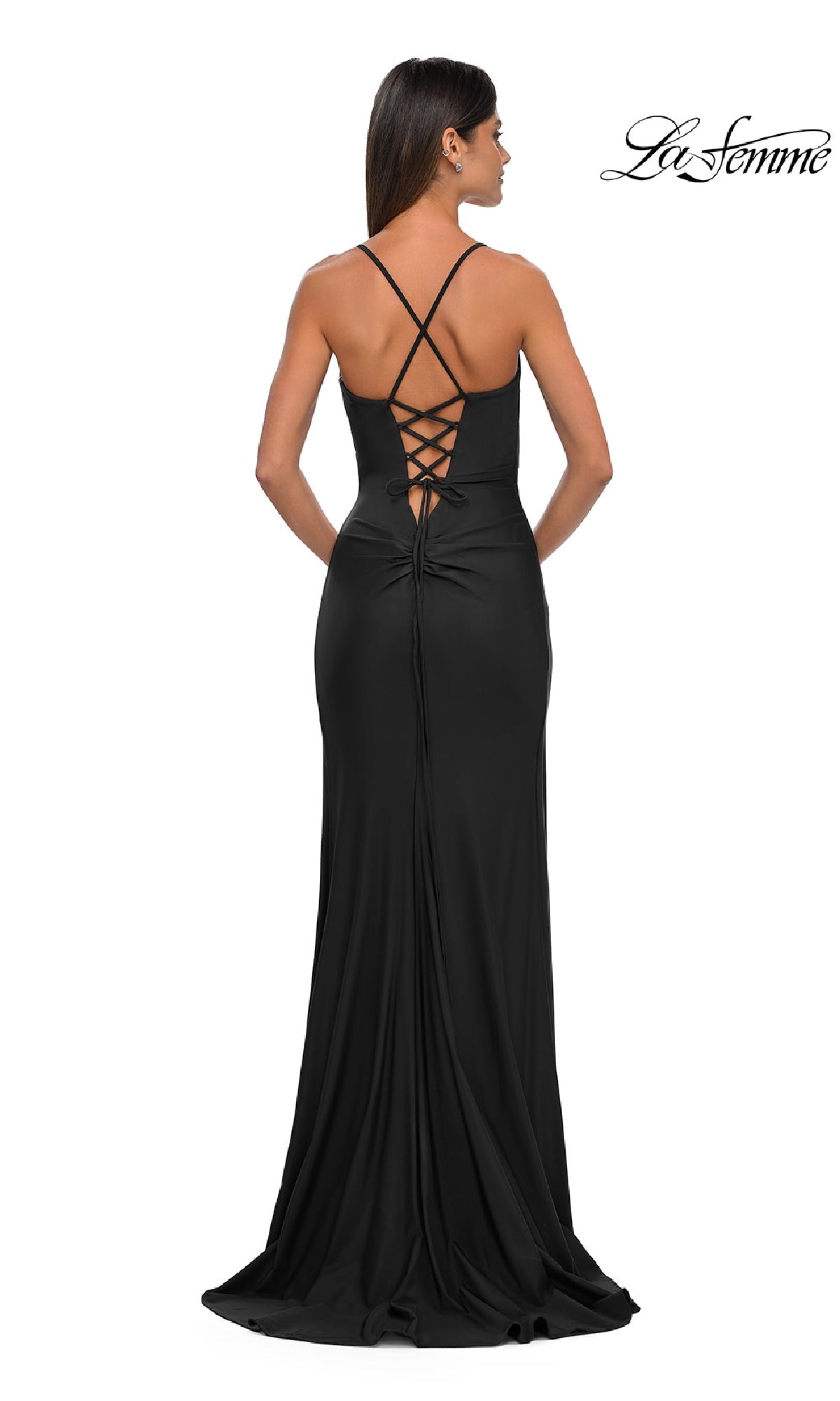 A woman stands with her back to the camera in the Lace-Up Simple Long Prom Dress: La Femme 33103, a black formal gown with thin straps, a crisscross lace-up back, fitted silhouette, and a slight train.